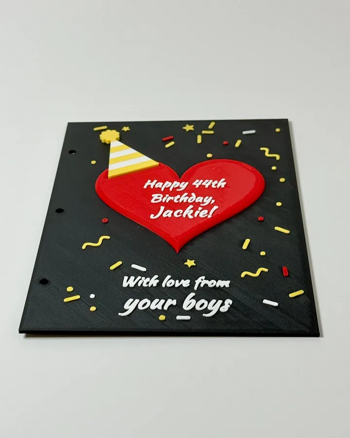 A 3D printed birthday card: a red heart with a striped party hat and confetti, reading Happy 44th Birthday, Jackie! With love from your boys