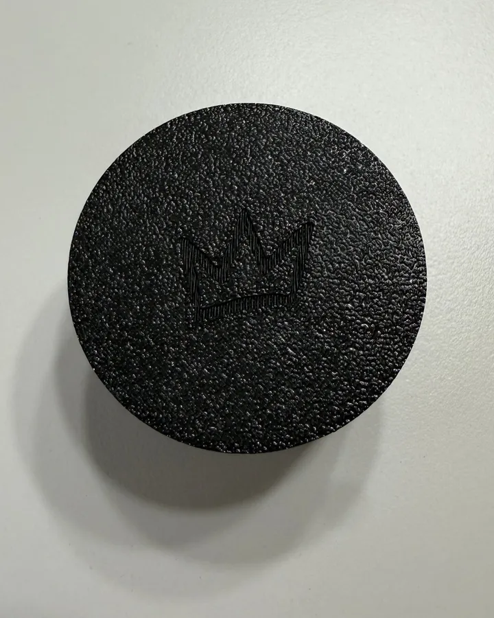The textured bottom of a black clicker with a small Prince Friends crown pressed into it