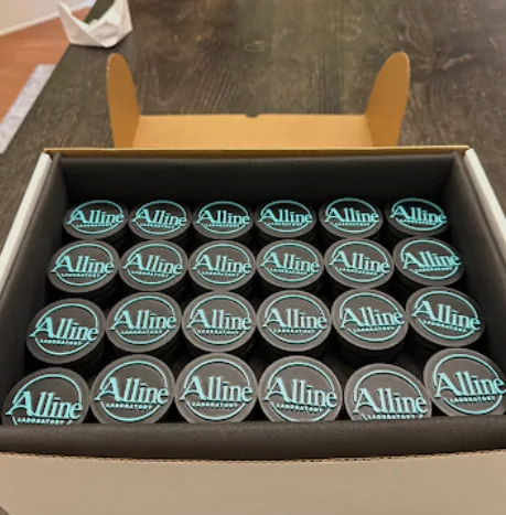 Two dozen finished Alline clickers packed in rows in a shipping box