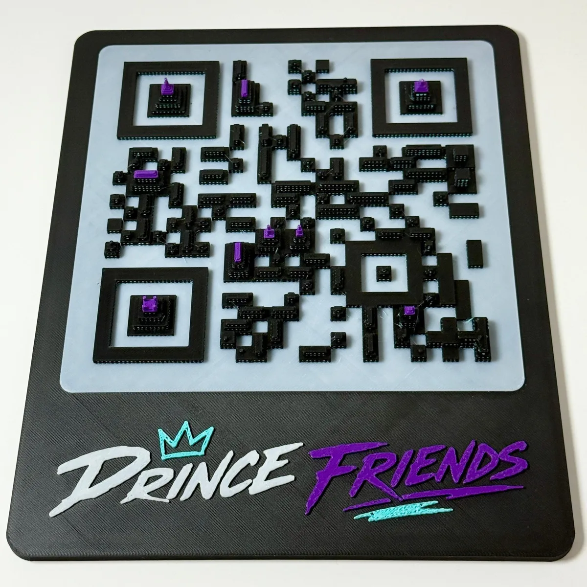 Our 3D printed QR code sign, straight on: the code built as a tiny black city on white streets, with purple rooftops and the Prince Friends logo underneath